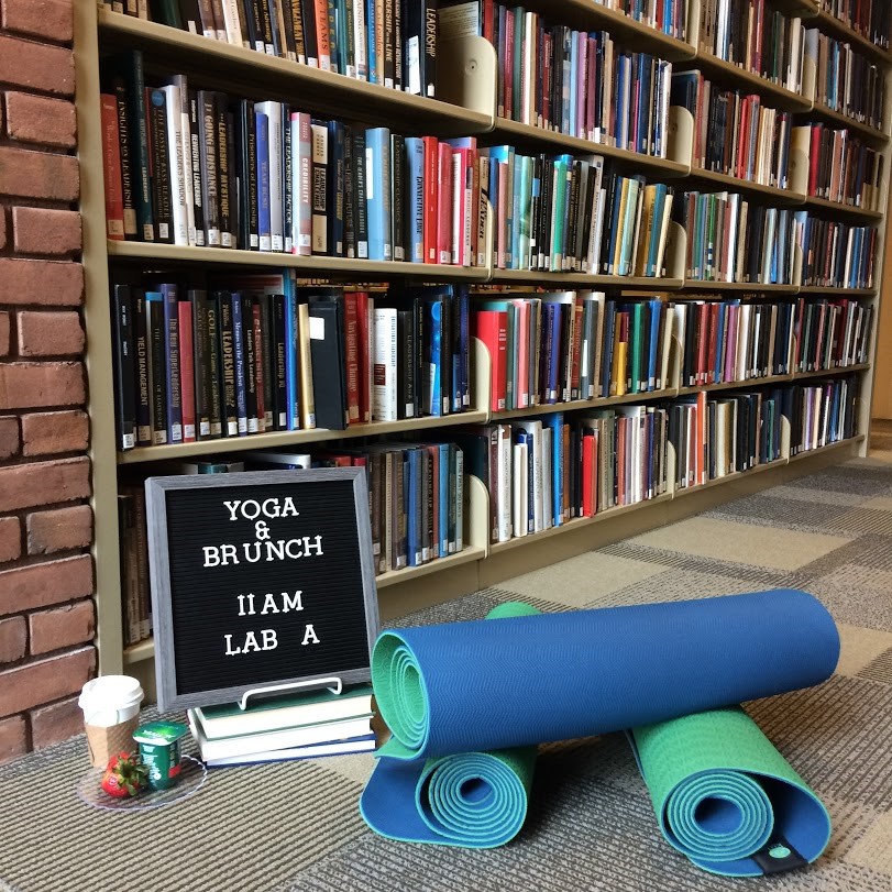 Library shelf with display of yoga mat, sign, coffee, and strawberries. 