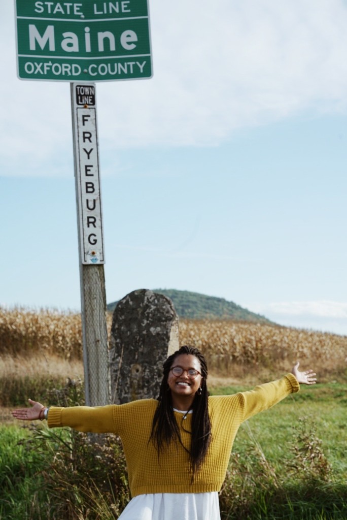Mallory Walker standing in front of a signpost at the Maine state line.