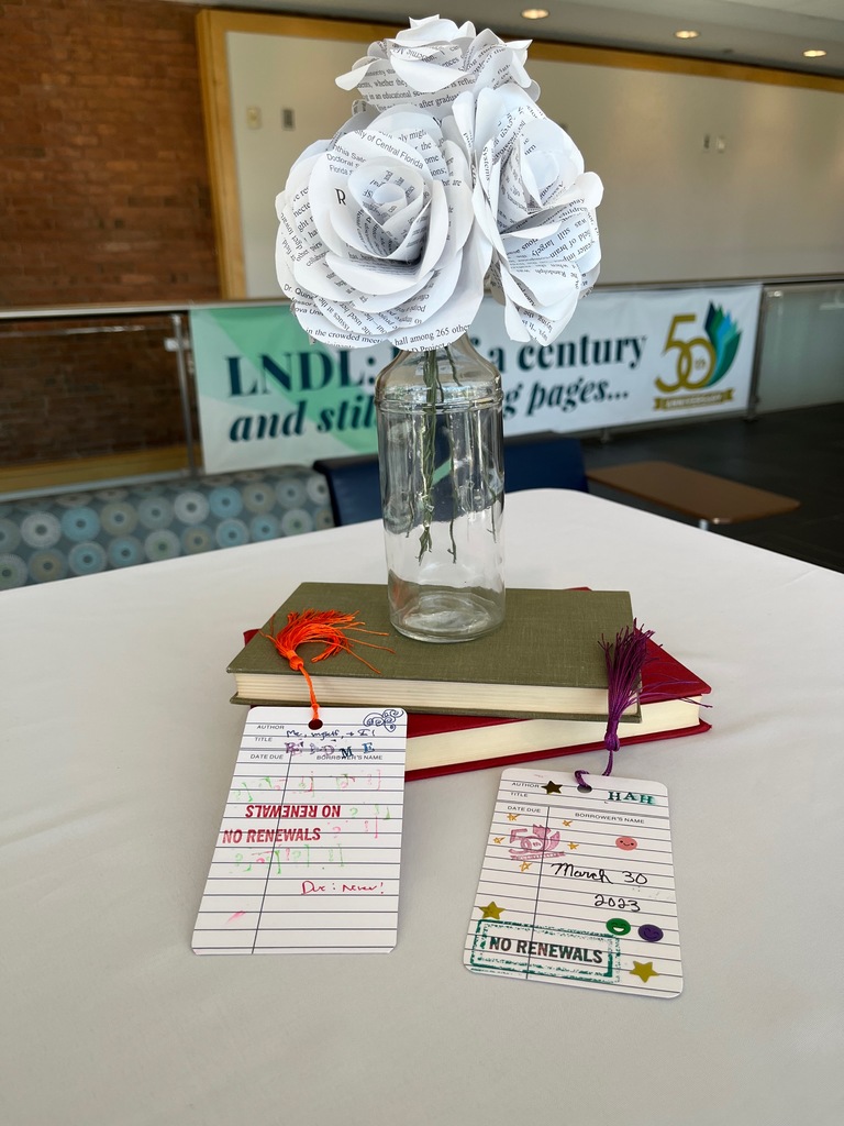 Paper flowers made from book pages dispalyed alongside a library due date card craft table at the 50th anniversary celebration
