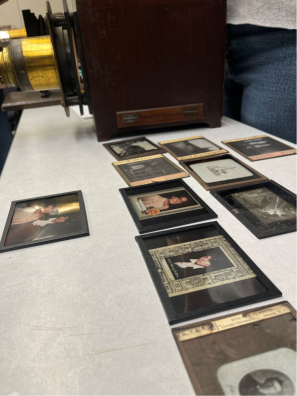 An array of magic lantern slides on a table beside a magic lantern