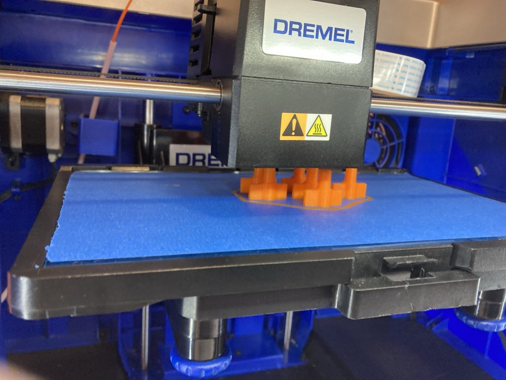 Dremel 3D printer in process of 3D printing orange plugs for IV bags