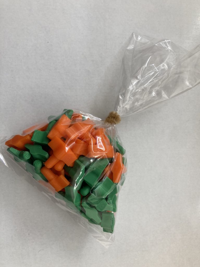 Plastic bag with finished orange and green 3D printed IV bag plugs. 