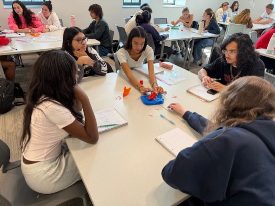 Students around a table interchanging different parts of the two 3D printed ships 